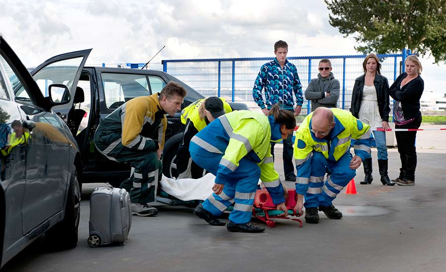 An emergency team carries a car accident victim on a stretcher, bystanders on the side​
